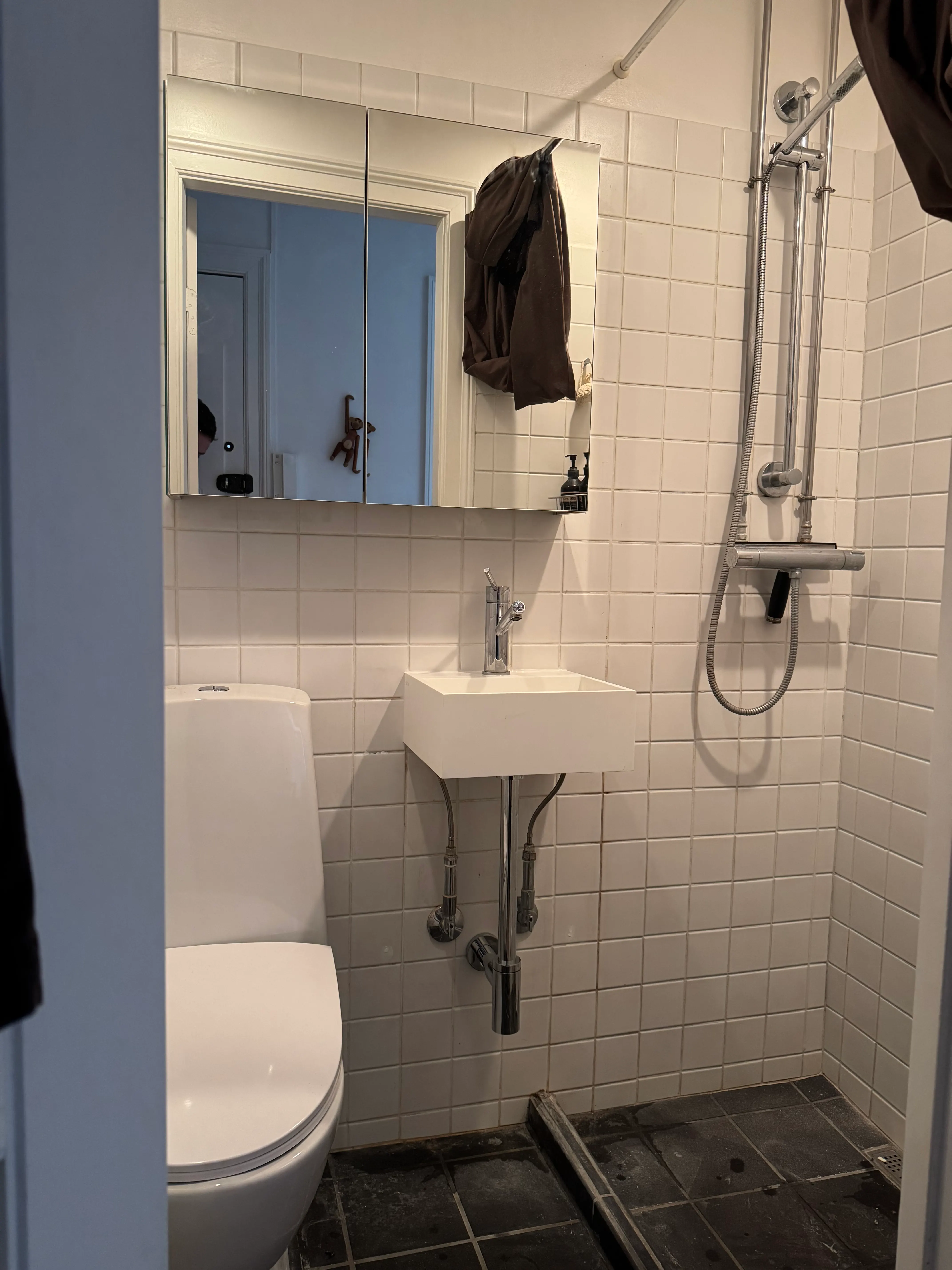 Completed bathroom with compact wall-mounted sink, mirrored cabinet and visible plumbing
