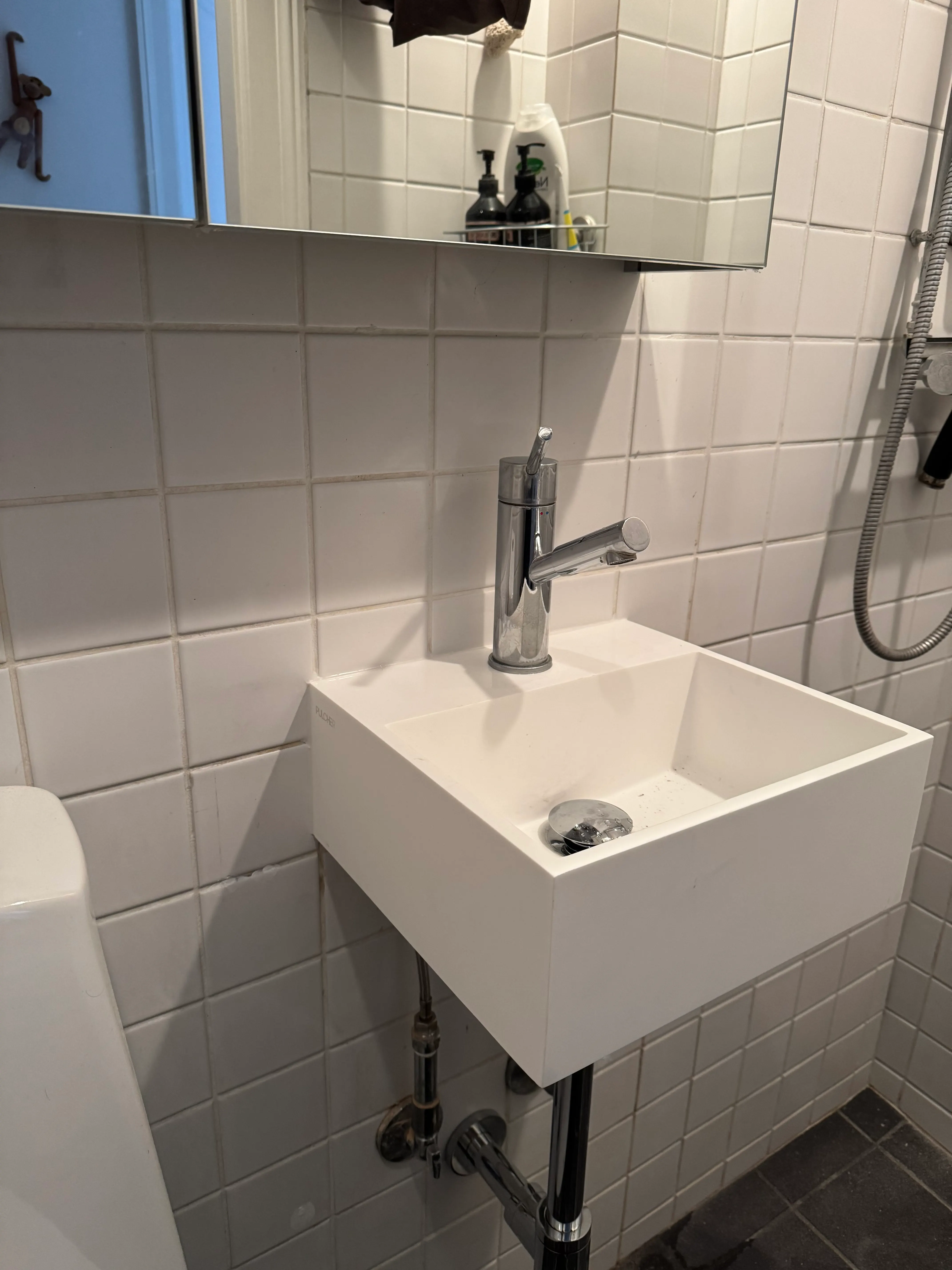 Compact wall-mounted bathroom sink below a large mirrored cabinet in a tiled Frederiksberg bathroom