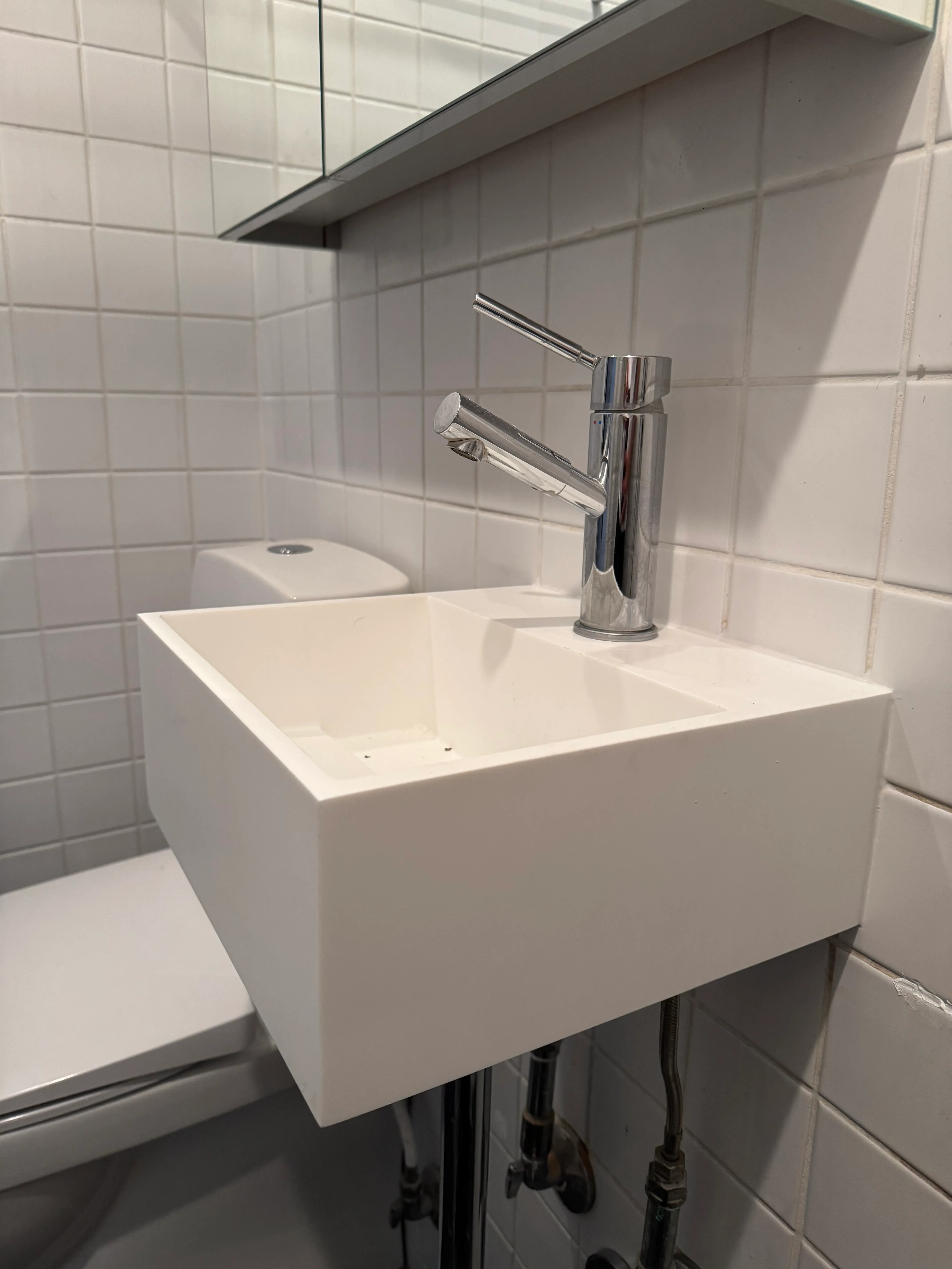 Side view of compact wall-mounted bathroom sink beneath a mirrored cabinet
