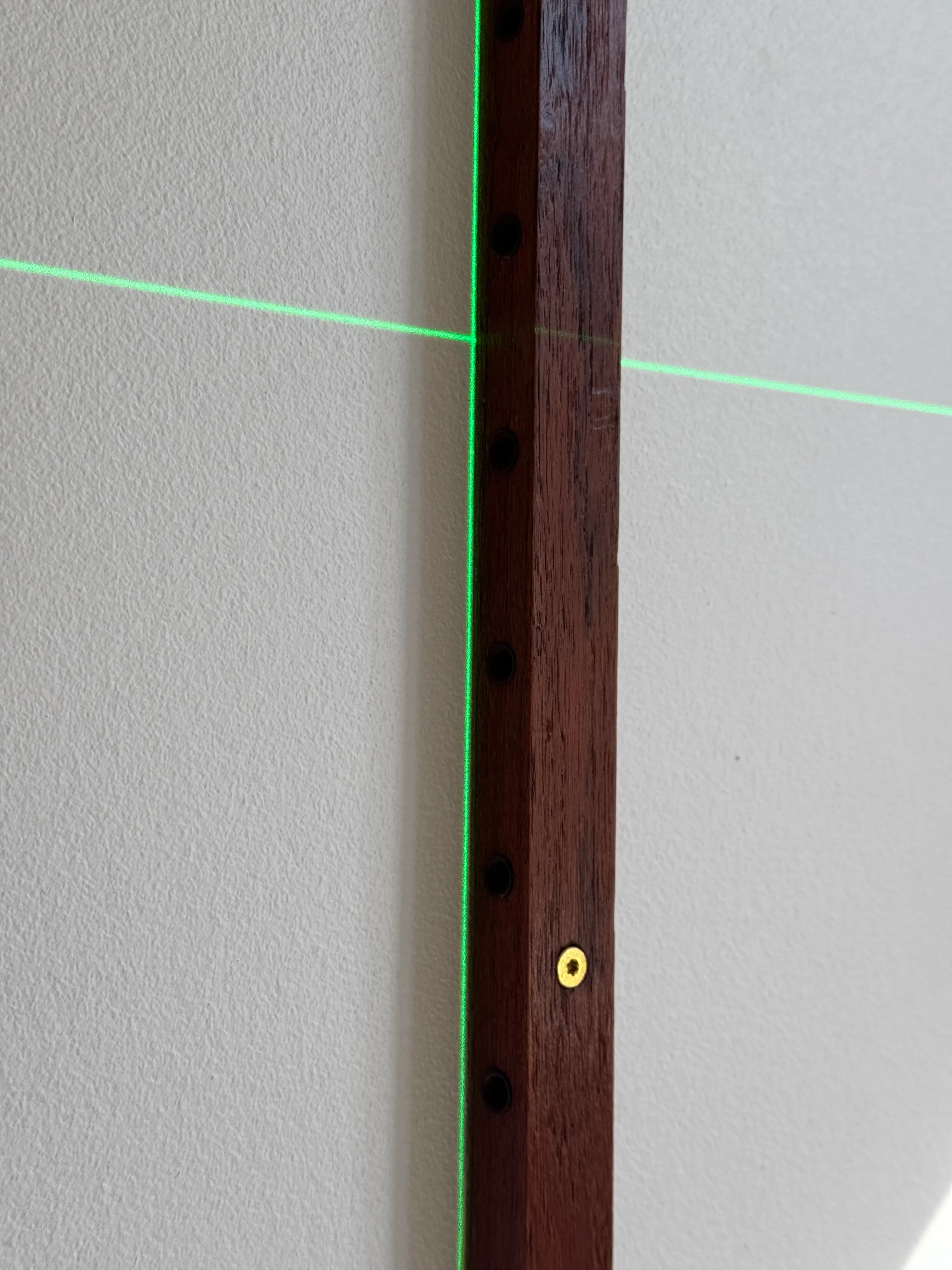 Laser alignment line across a timber Cadovius wall rail with a gold-coloured fixing head