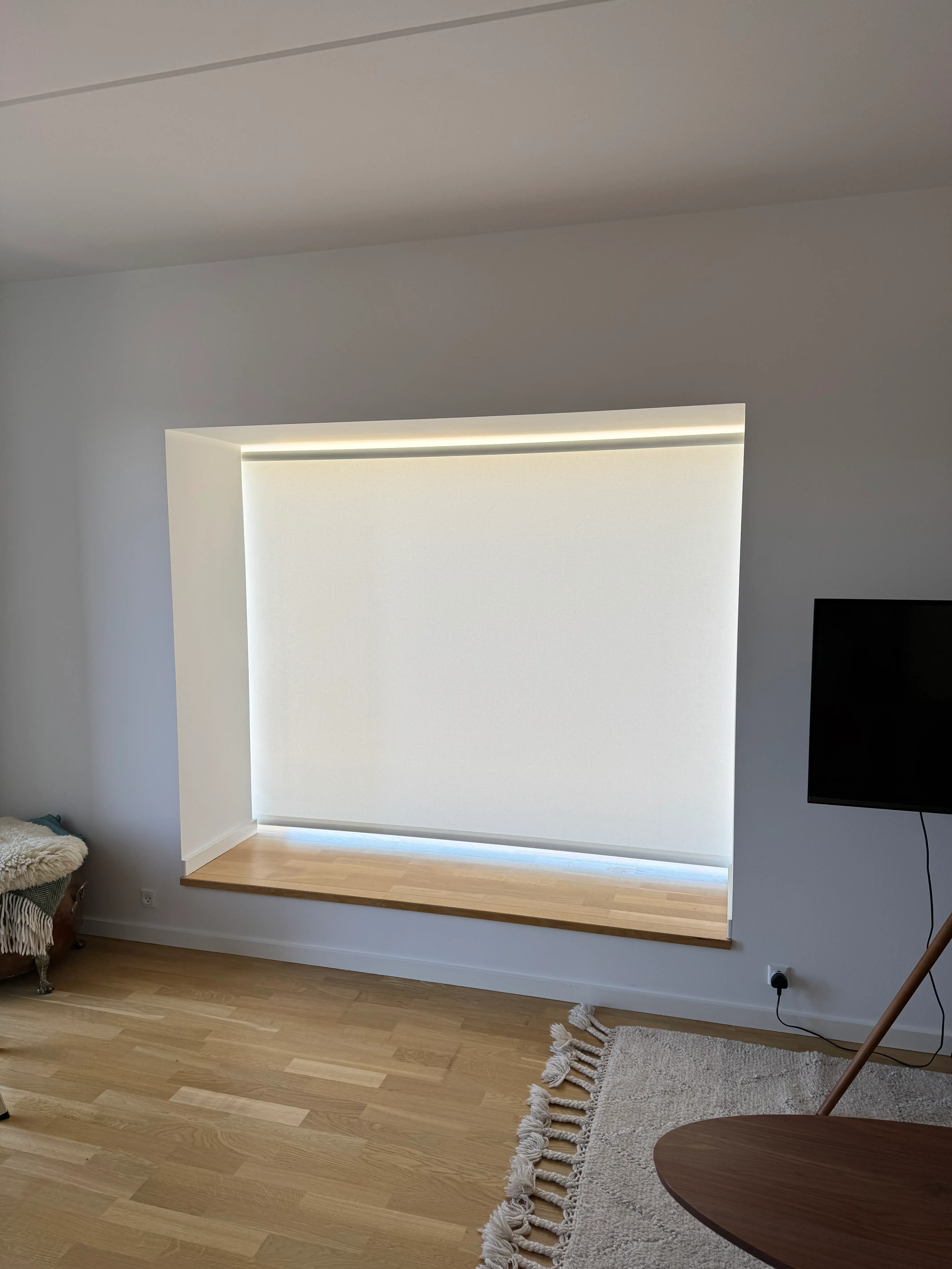 Wide roller blind installed inside a broad living-room window recess in Valby